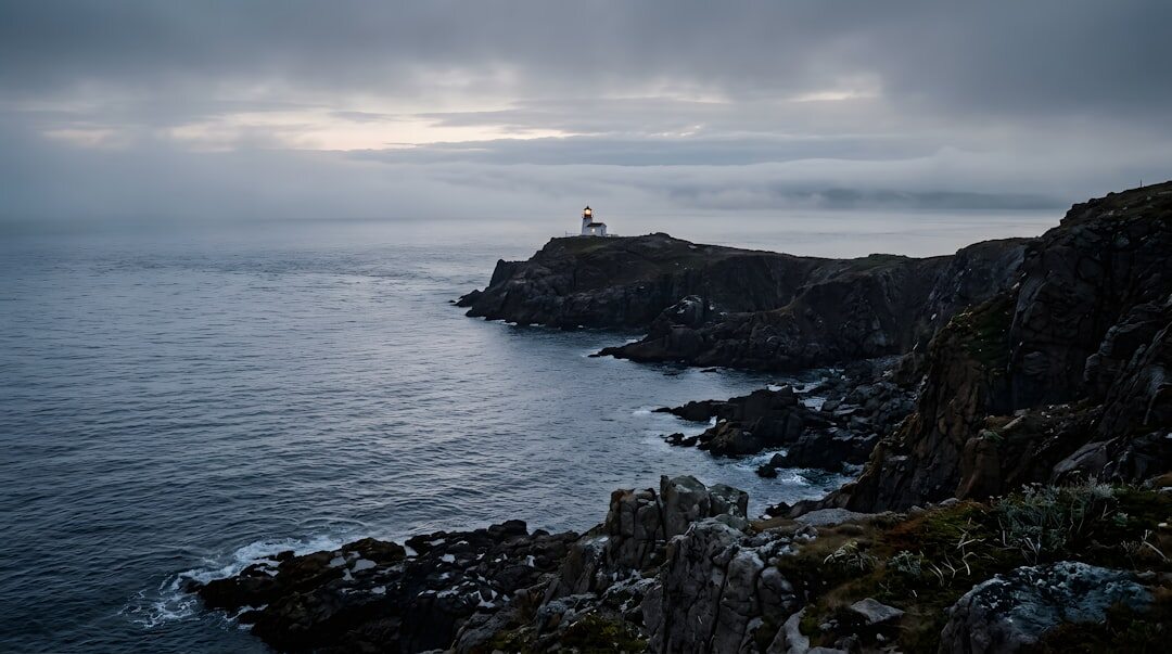 Lonely lighthouse on a foggy rocky coastline at dusk