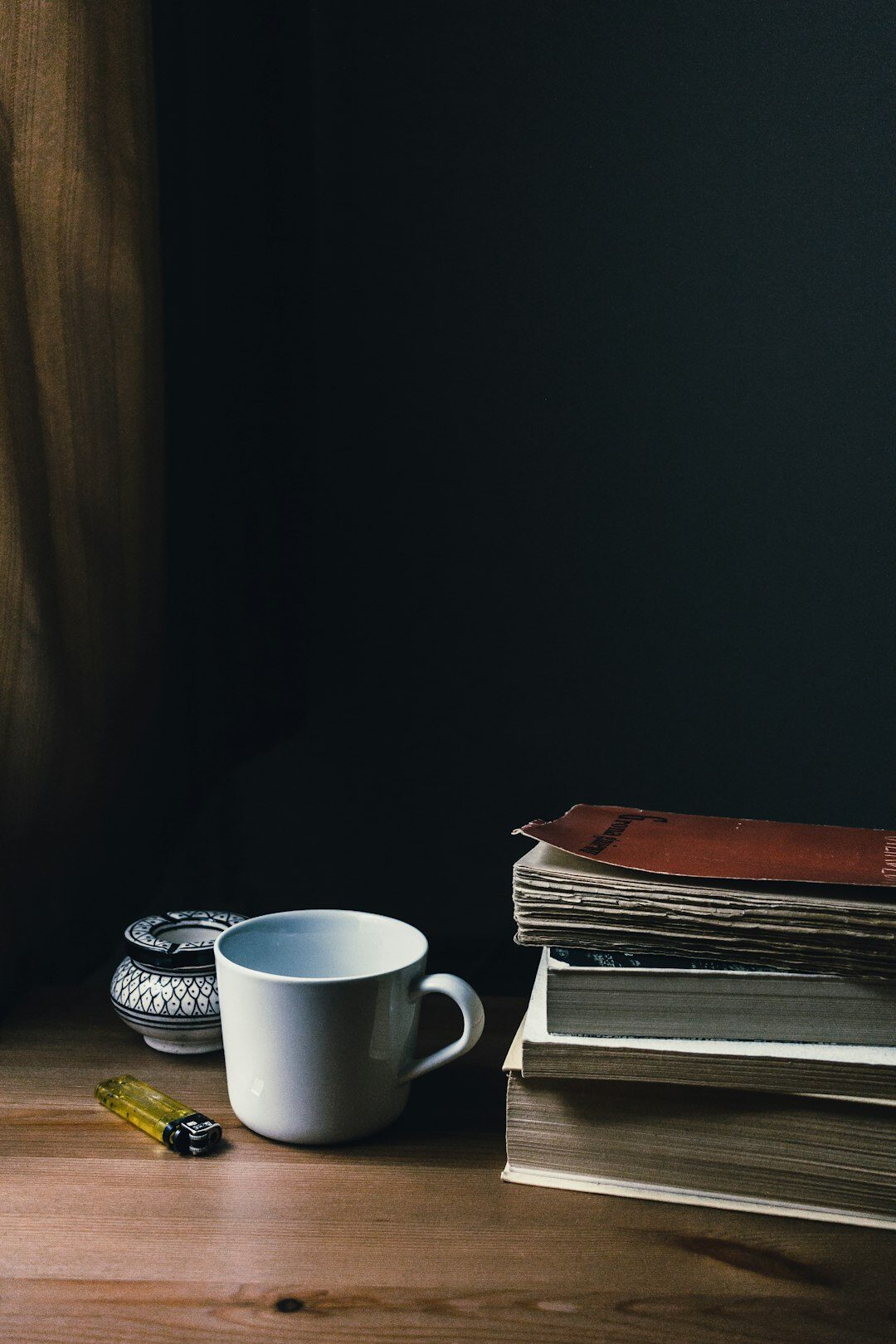Stack of old books with a cup of coffee and notebook on a wooden desk